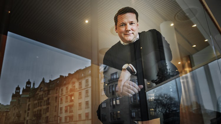 Tobias Baudin sitter vid ett fönster som speglar byggnader i centrala Stockholm