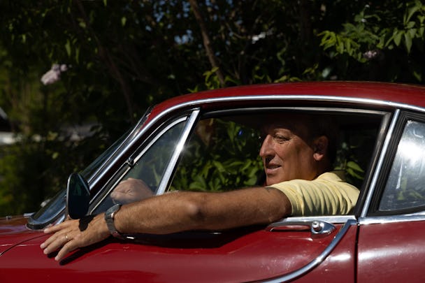 Stefan sitter med armen ut genom fönstret på sin röda Volvo P1800 S.