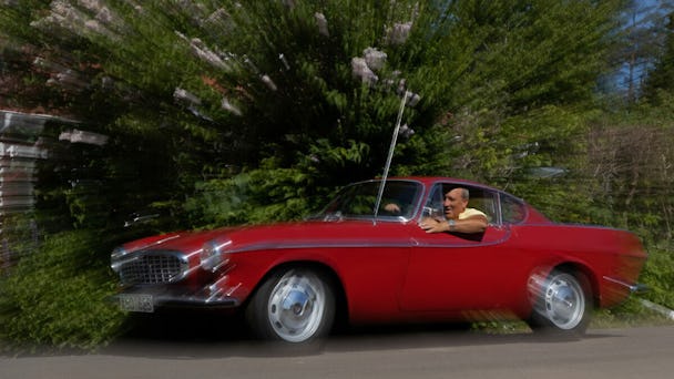 Stefan Andersson sitter i en gammal och röd sportbil.
