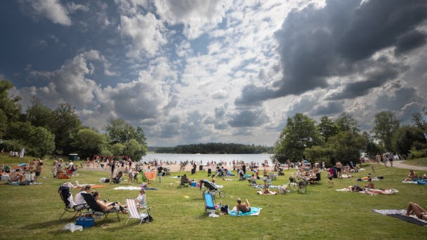 Folkmassa som njuter av en solig dag i en park vid en sjö.