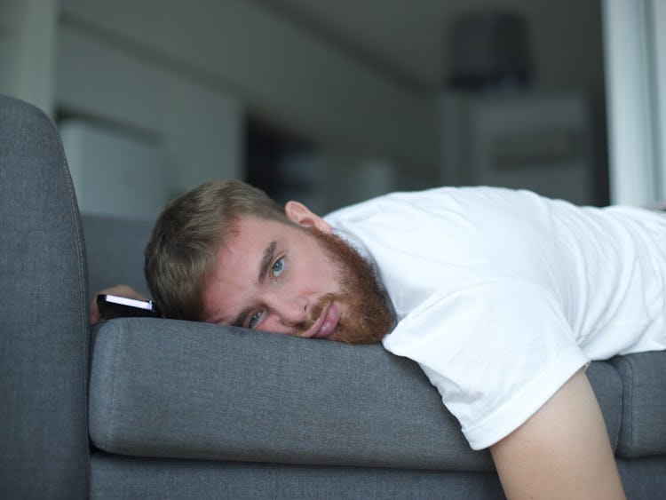 En man vilar huvudet på en soffa med ett fundersamt uttryck.
